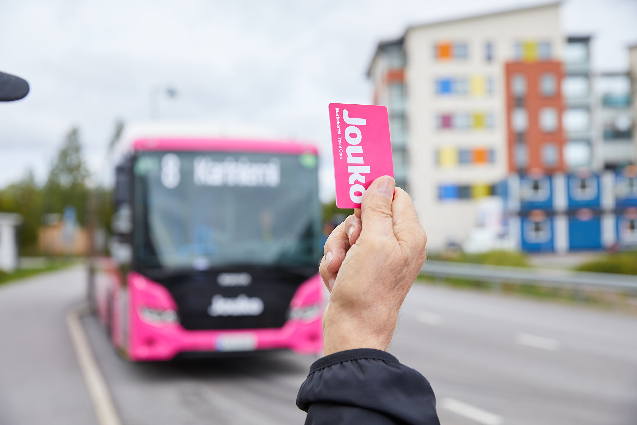 Henkilö heiluttamassa pinkkiä bussikorttia bussille.