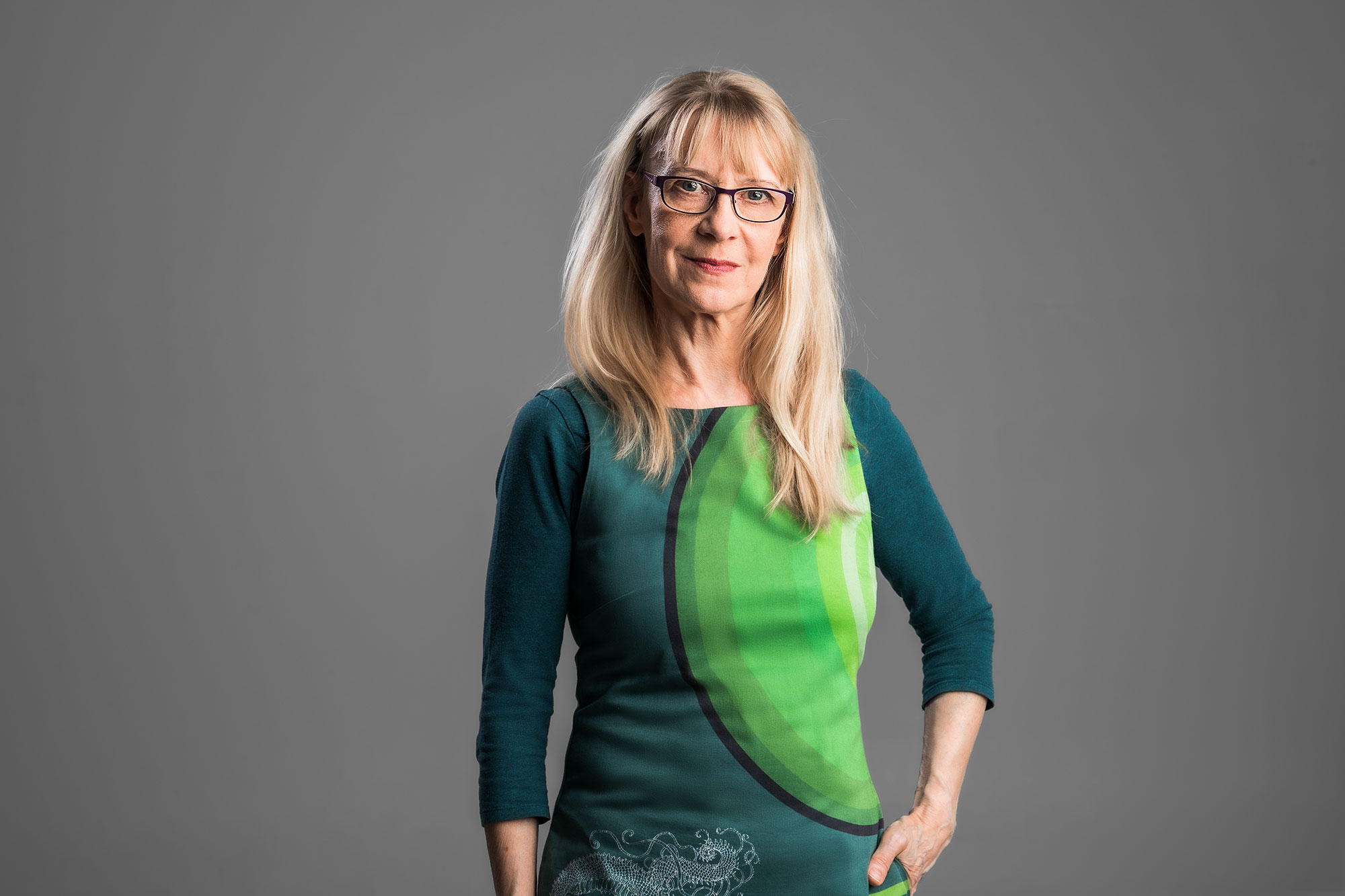 Kuva Helka-Maria Kinnusesta; vaalea hiuksinen nainen, jolla on silmälasit ja vihreä paita katsoo kameraan.