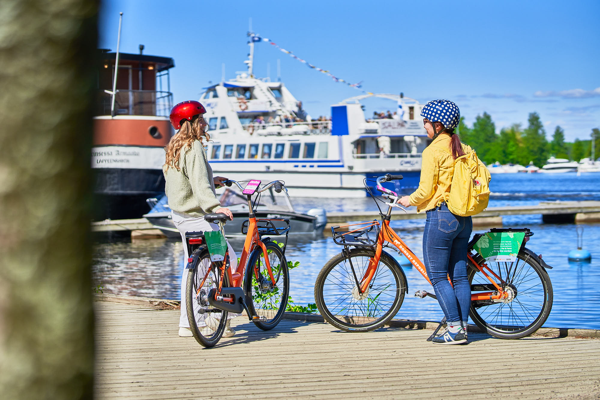 Kaksi nuorta Lappeenrannan satamassa pyöräilykypärät päässä kaupunkipyörien vierellä, taustalla Saimaa ja aluksia.