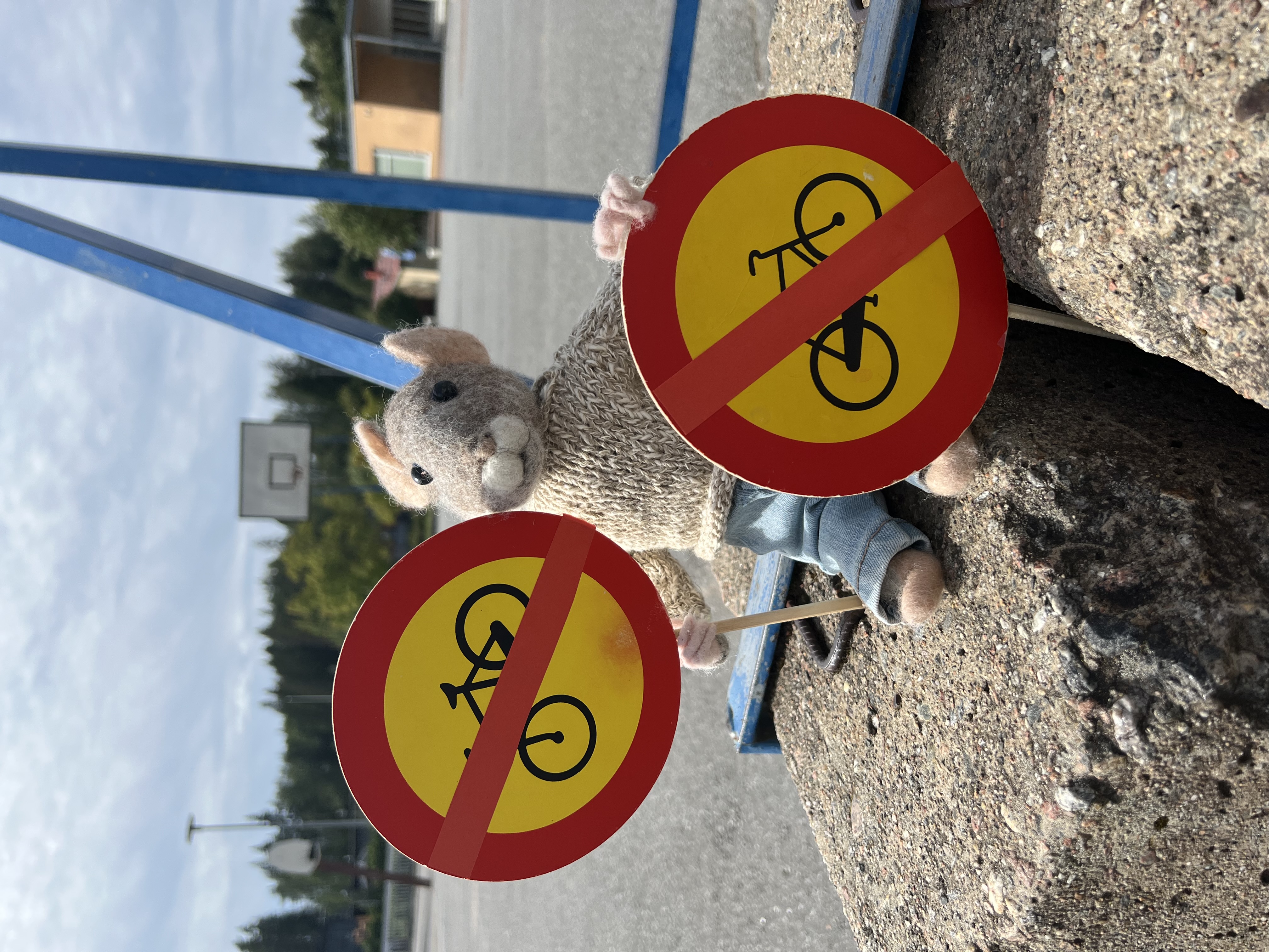 Koulun maskotti Hipsu-hiiri pitää tassuissaan kahta "Pyöräily kielletty" -liikennemerkkiä.