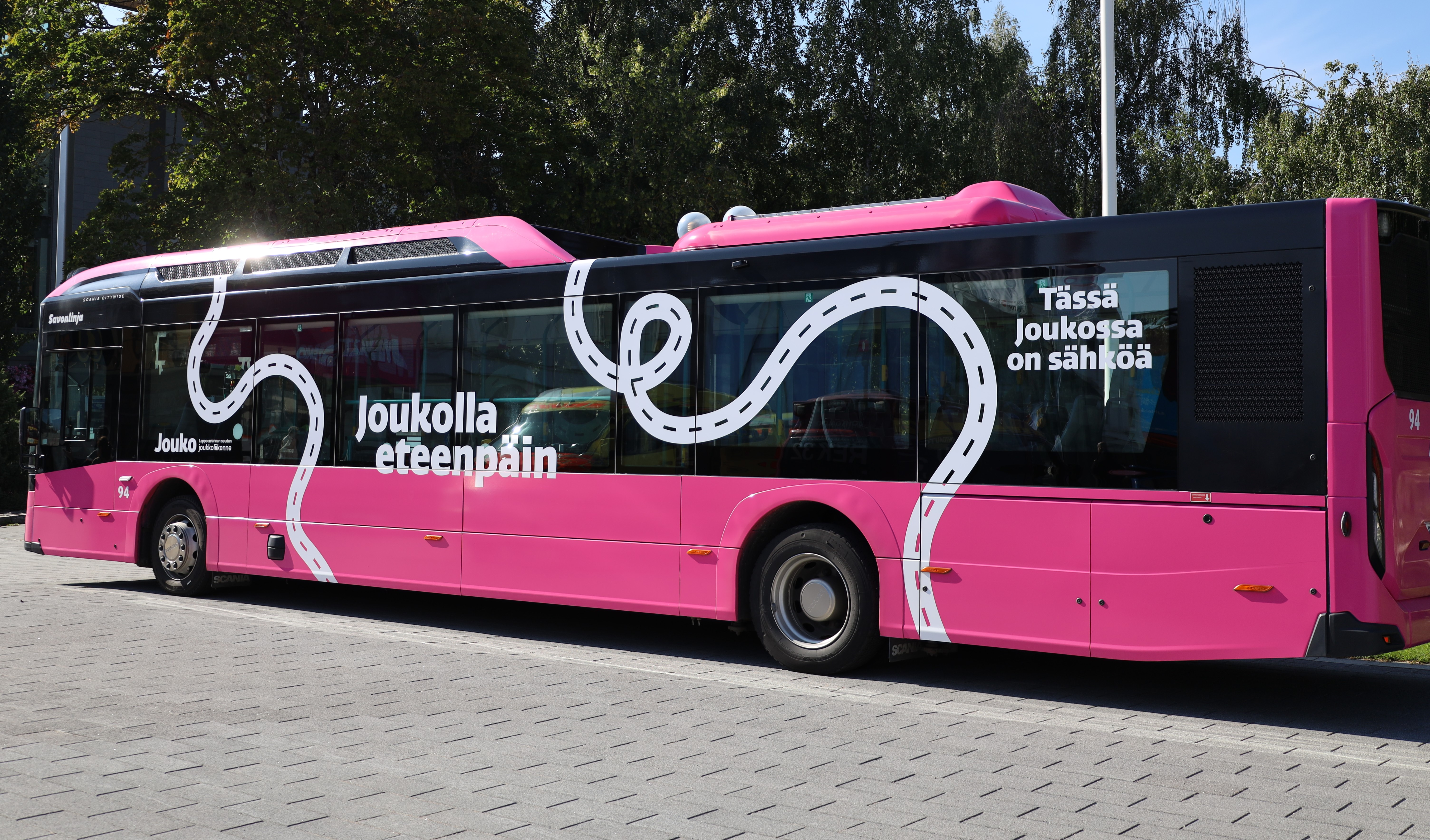 Pinkki Jouko-bussi, jossa lukee ”Joukolla eteenpäin” ja ”Tässä Joukossa on sähköä”.