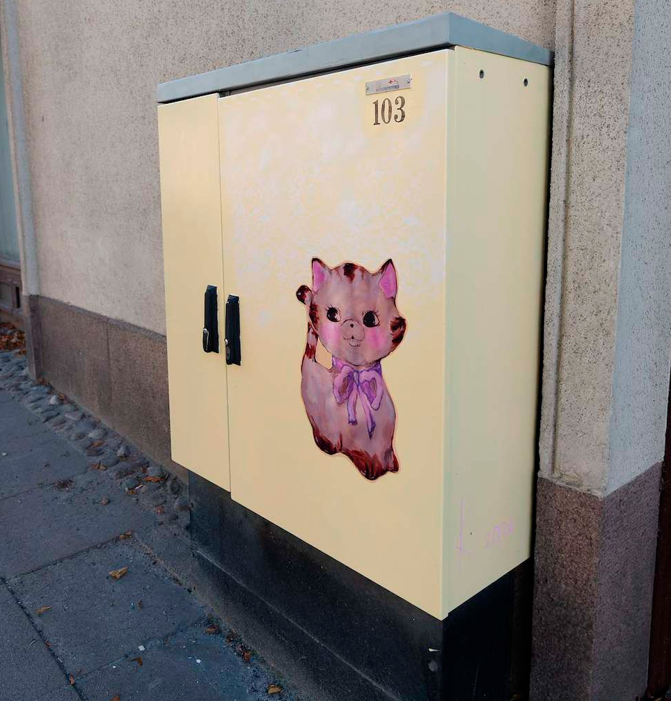 Keltaisen sävyisessä jakokaapissa on maalaamalla toteutettu posliininen kissa.