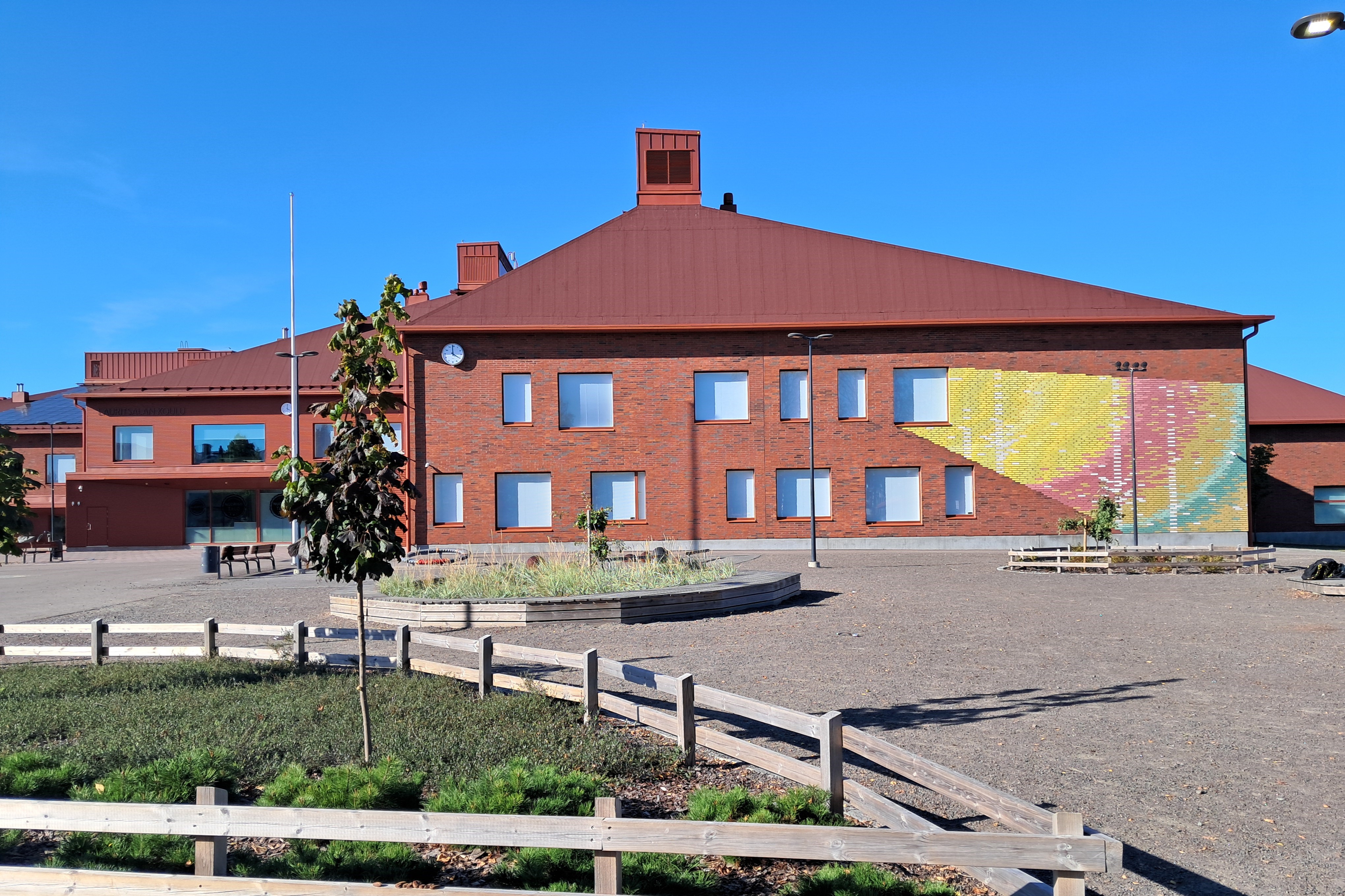 Punertava rakennus ja piha-aluetta aurinkoisena kesäpäivänä.