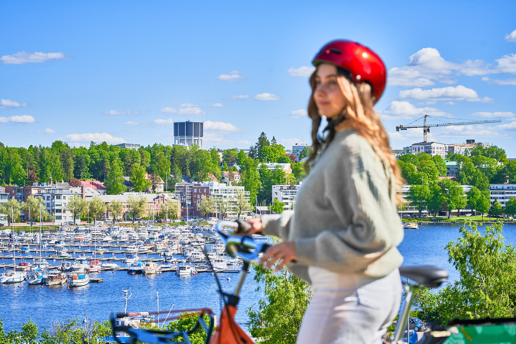 Etualalla pyöräilijä Linnoituksessa aurinkoisena kesäpäivänä. Taustalla Lappeenrannan Kaupunginlahti ja veneitä.