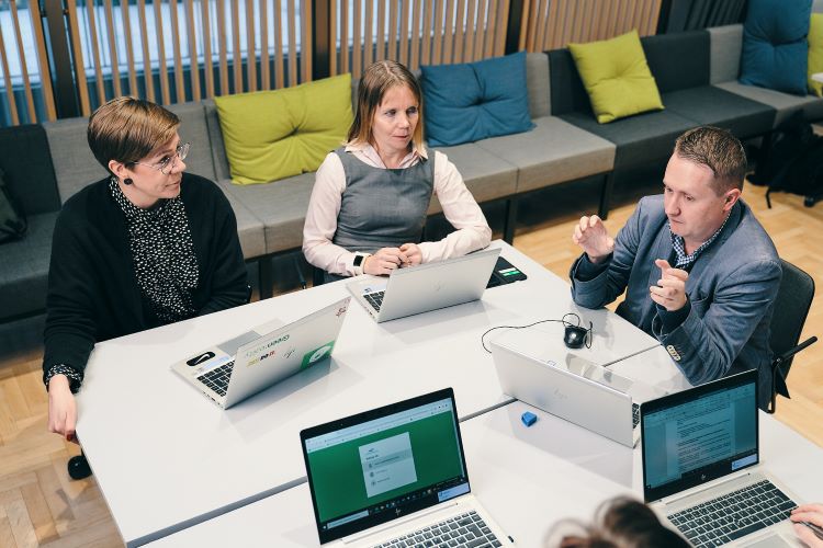 Pieni joukko ihmisiä tietokoneiden ääressä.