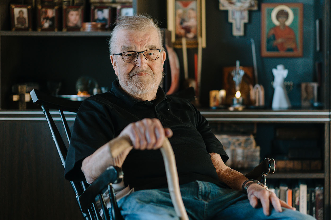 Matti J. Kuronen istuu tuolilla hyllykön edessä.