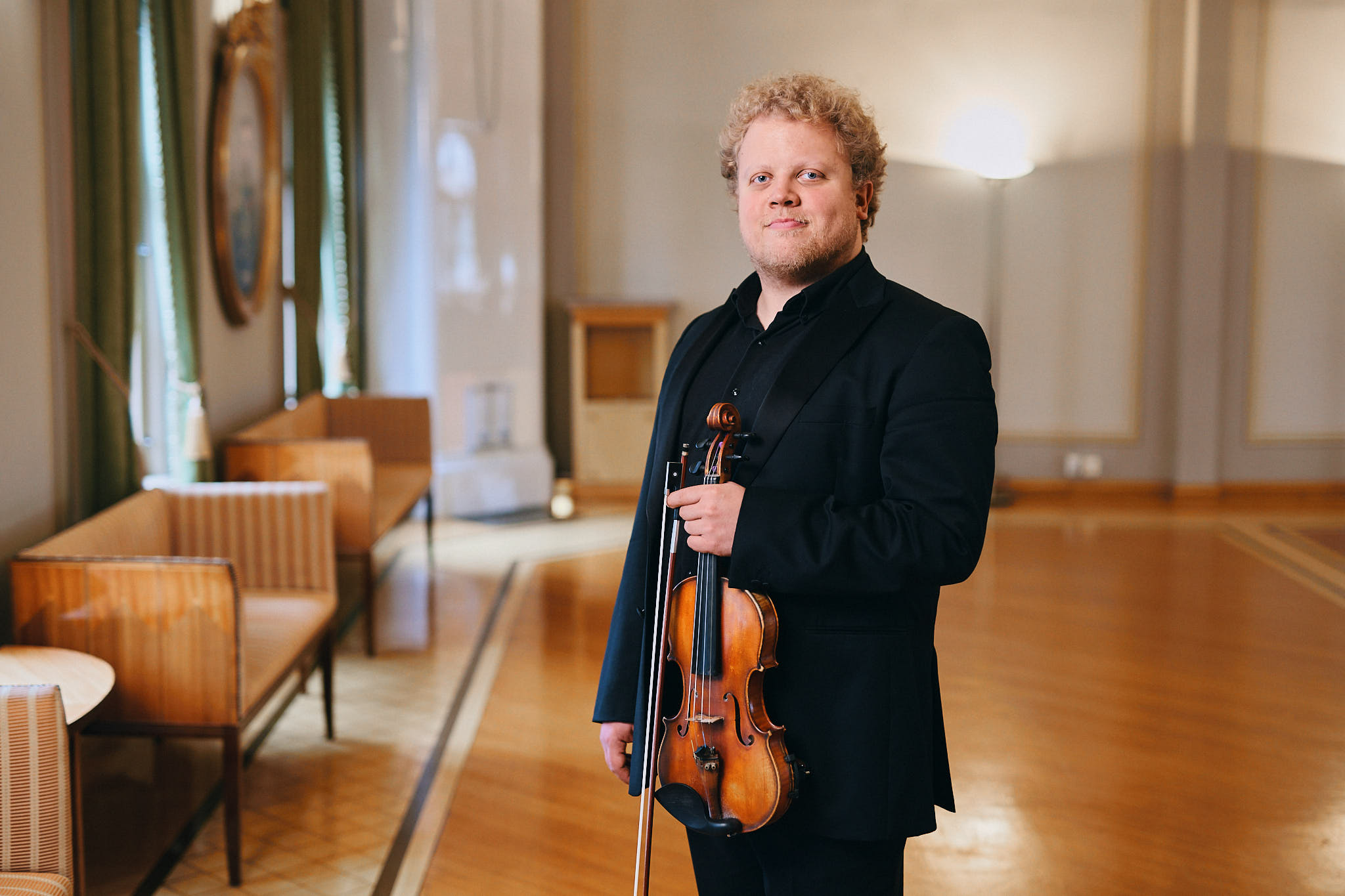 Mies seisoo viulu kädessä juhlasalissa.