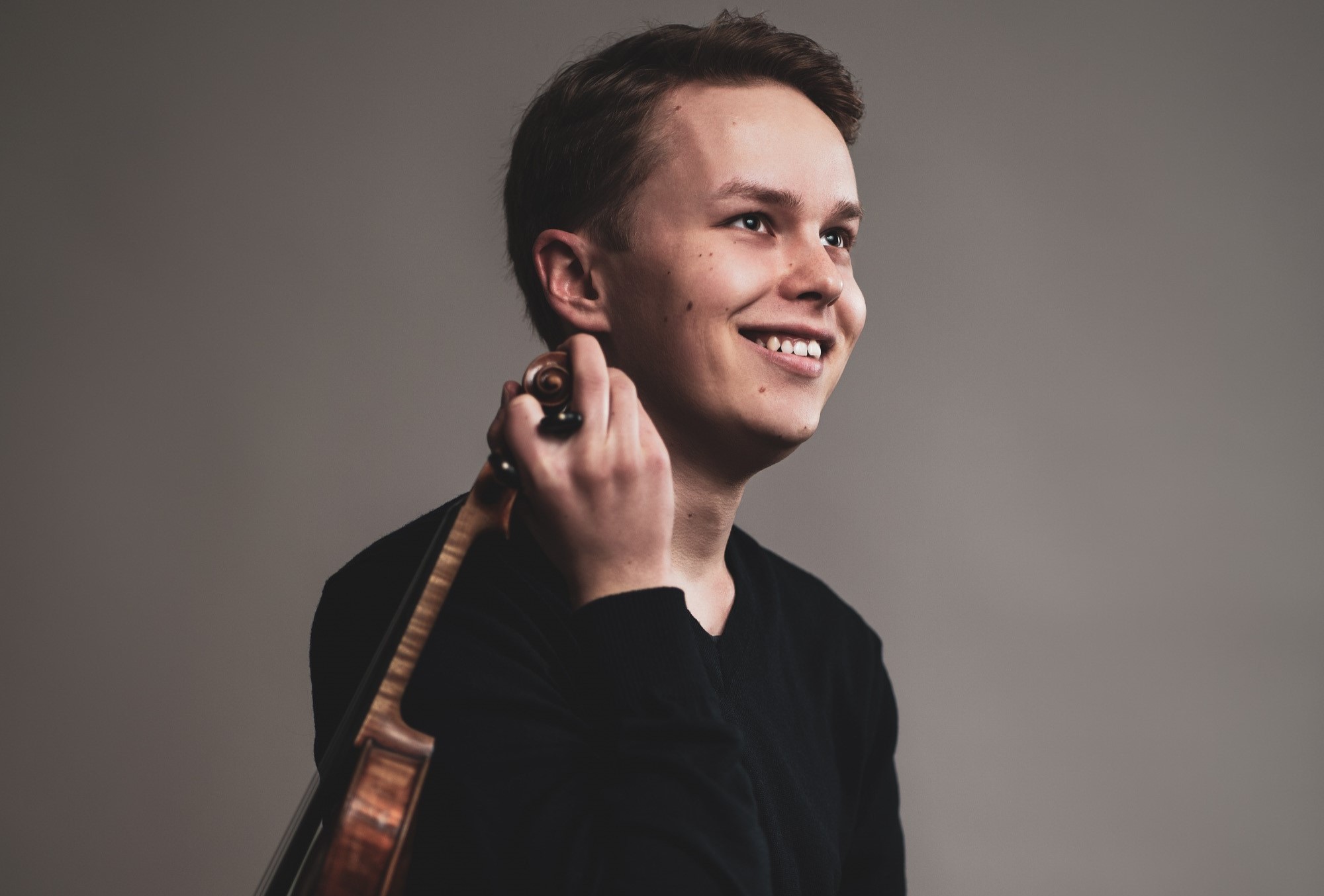 Hymyilevä nuori mies istuu ja pitelee kädessään viulua.