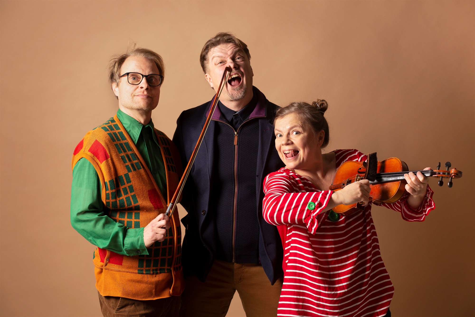 Leikkisässä kuvassa kaksi miestä ja nainen, jolla on kädessä viulu. Toinen miehistä pitelee kädessään jousea, jonka pää on toisen miehen nenässä.