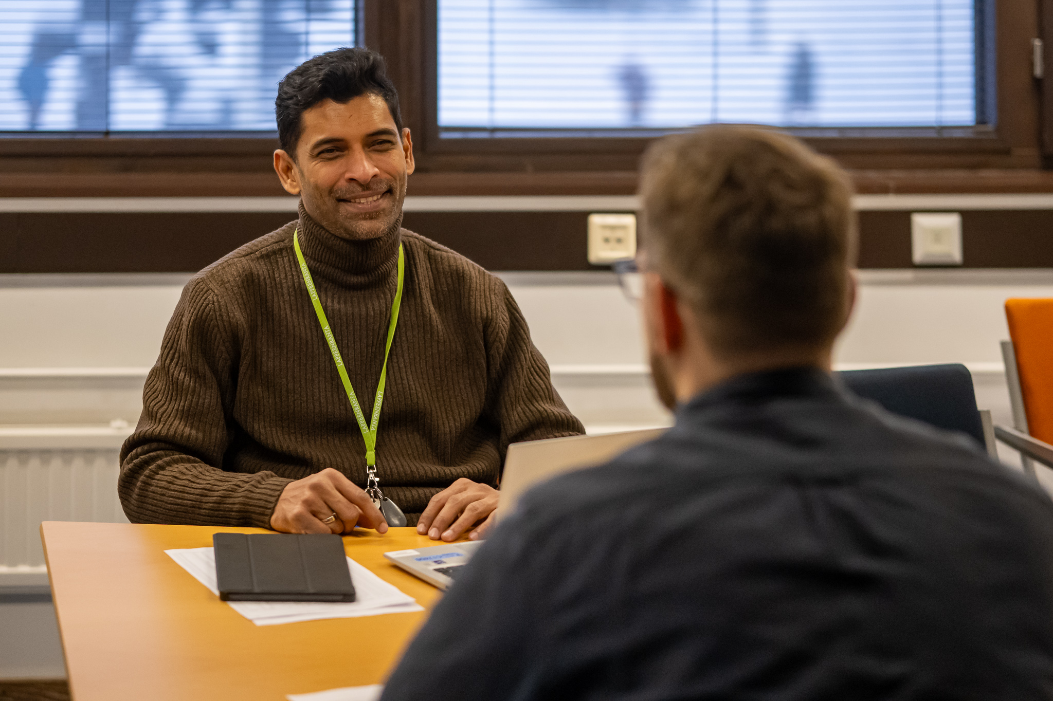 Kaksi mieshenkilöä istuu pöydän ääressä kasvotusten keskustelemassa.