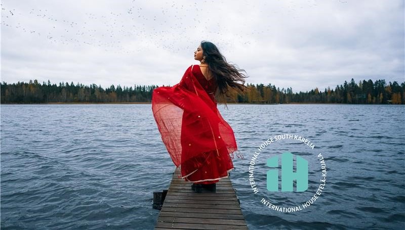 Naishenkilö seisoo laiturilla punainen mekko ja hiukset hulmuten.