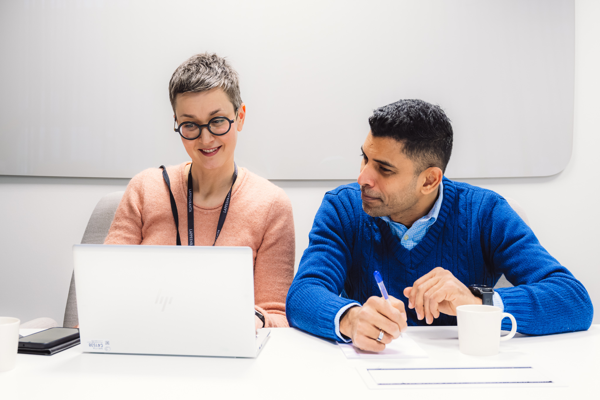 Nais- ja mieshahmo istuvat pöydän ääressä, edessään tietokone. He katsovat näyttöä yhdessä.