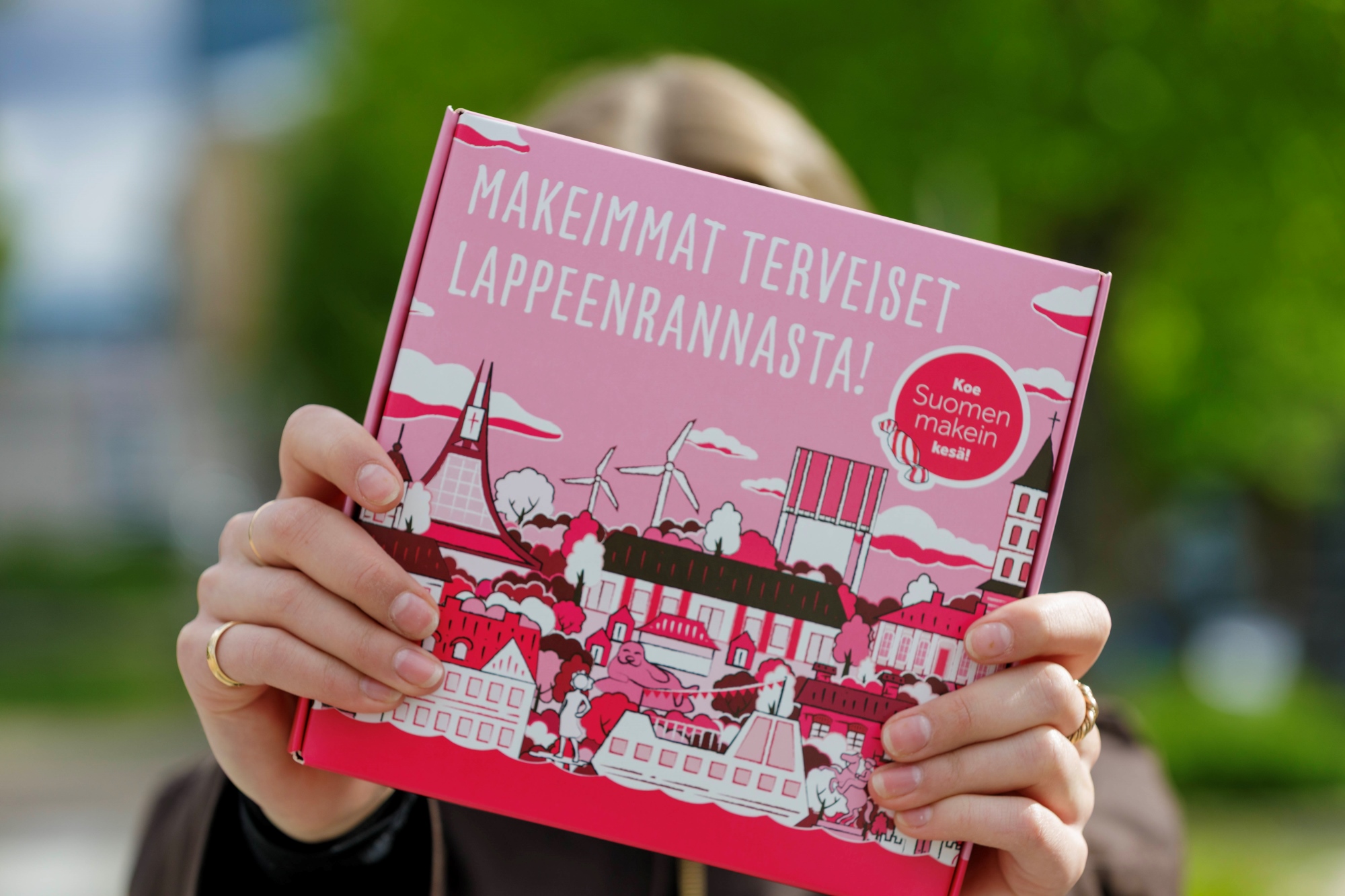 Henkilö pitelee Suomen makein kesä -karkkilaatikkoa kasvojensa edessä.
