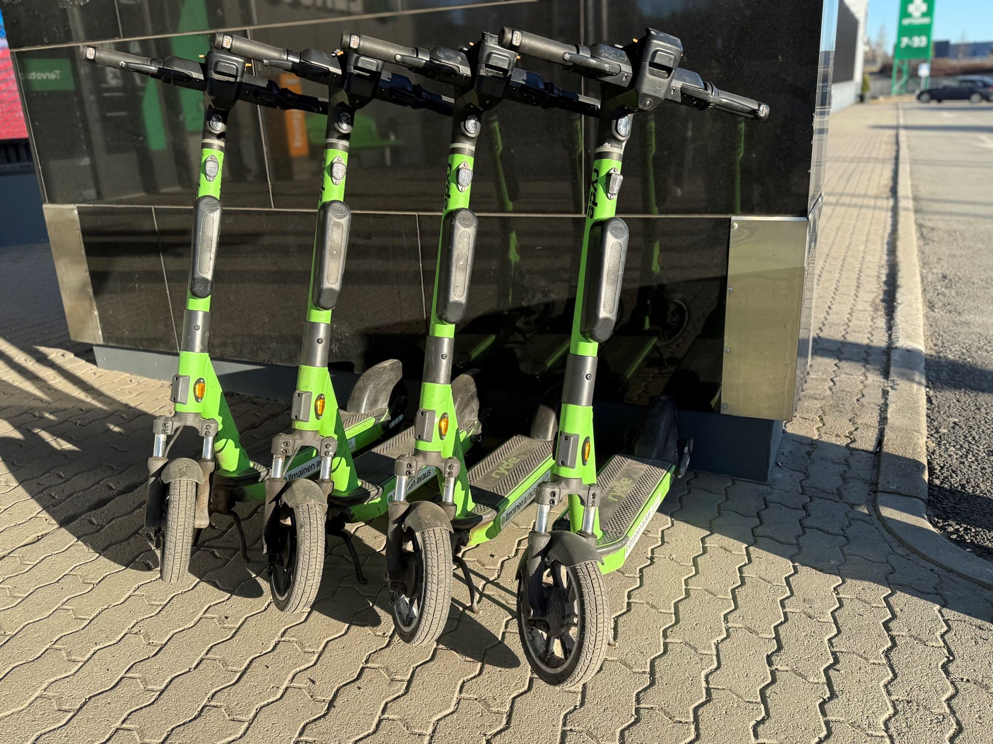 Neljä vihreää sähköpotkulautaa vierekkäin parkissa.