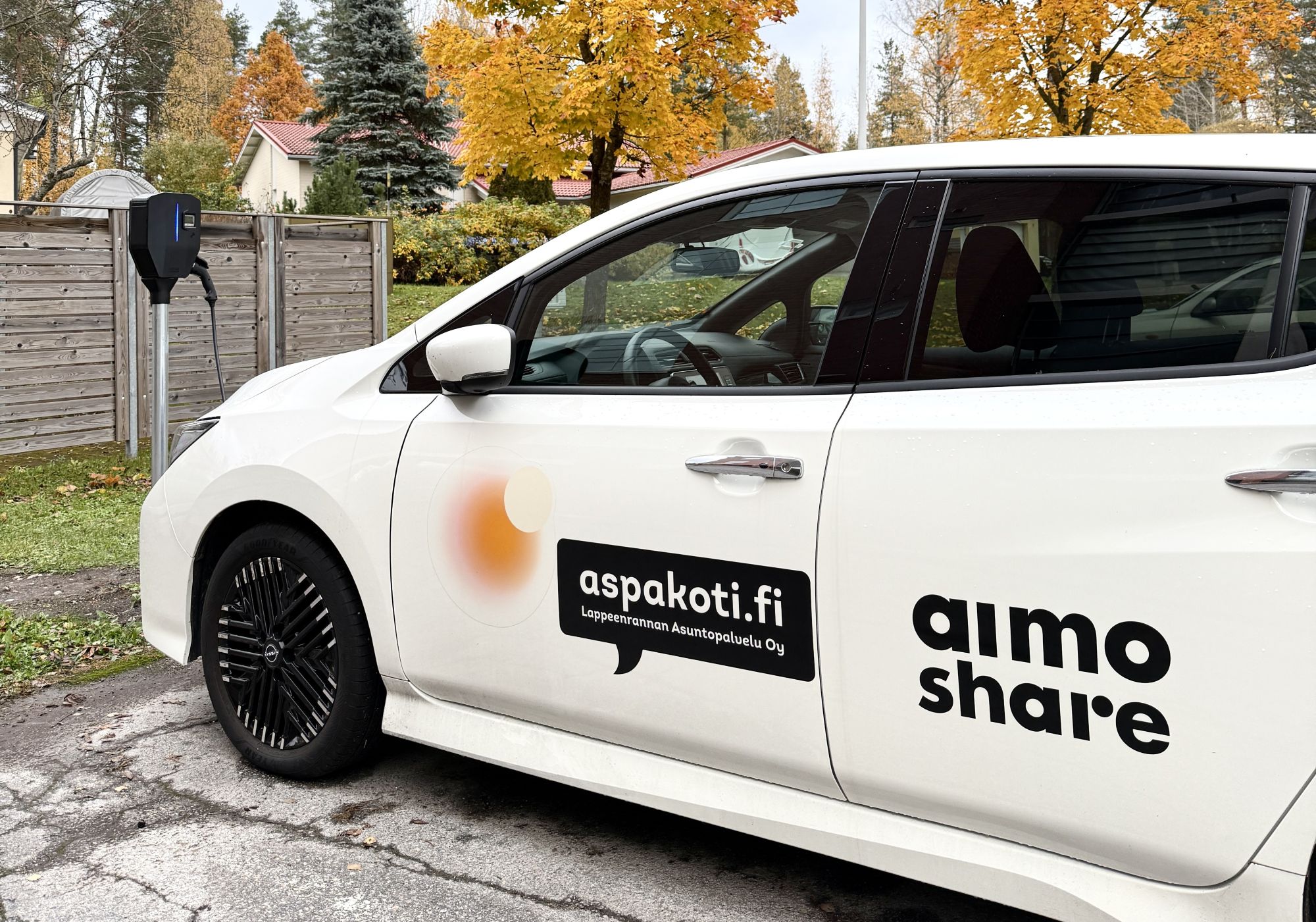 Valkoinen yhteiskäytössä oleva Aimo share -sähköauto latauspistokkeessa.