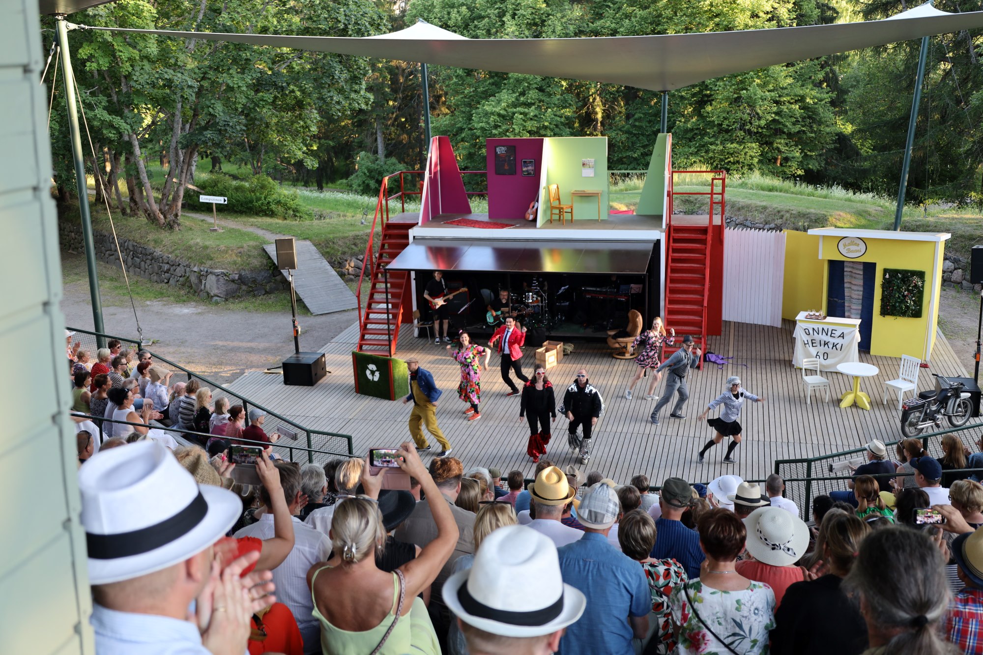 Lappeenrannan kesäteatterin yleisöä katsomossa sekä esitys käynnissä teatterin lavalla.