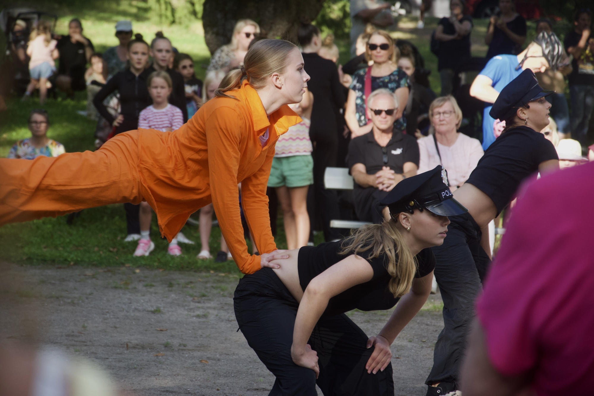 Yleisöä seuraamassa tanssiesitystä Lappeenrannan Pusupuistossa kesällä, tanssijat pukeutuneina poliiseiksi ja vangeiksi.