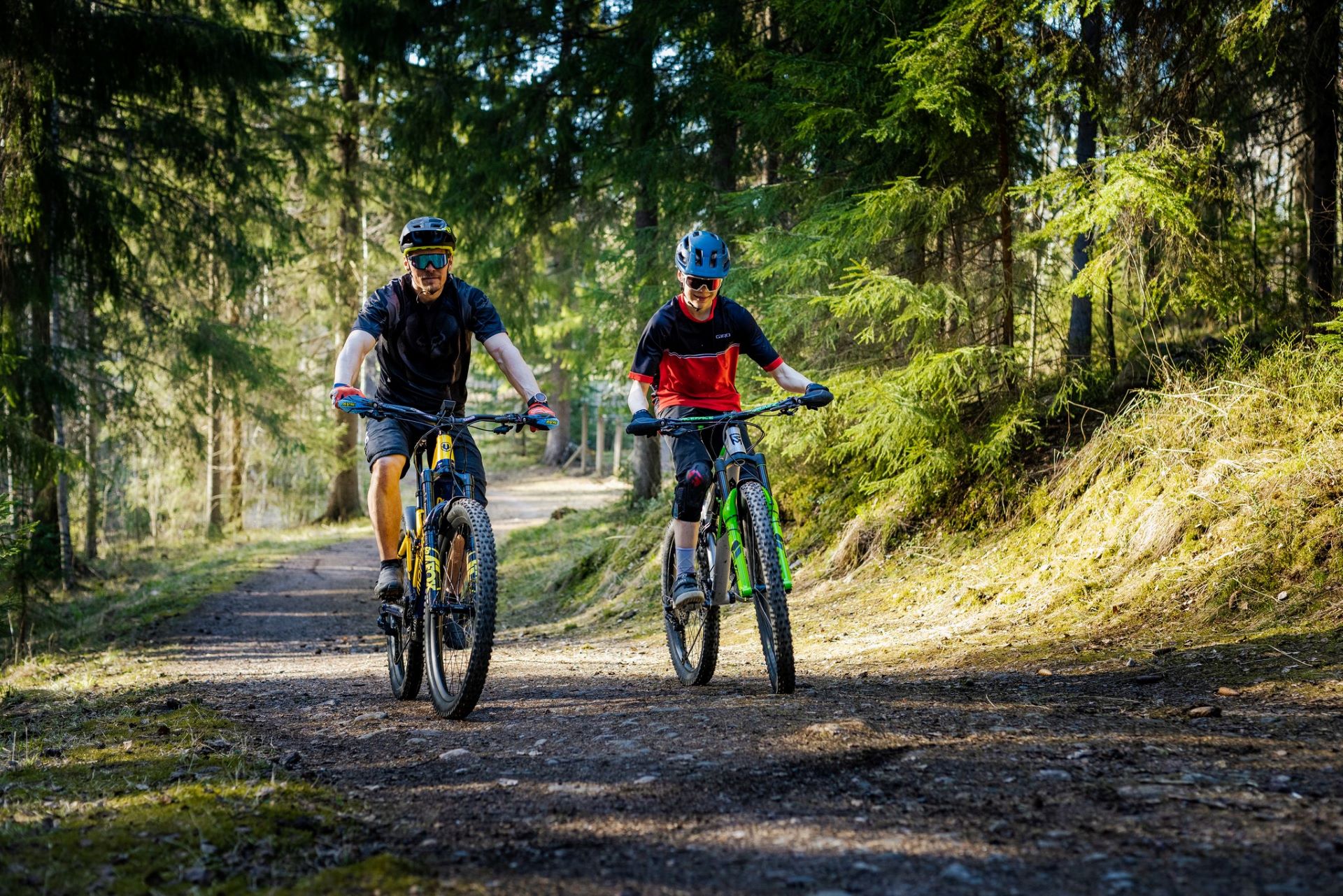 Kaksi maastopyöräilijää ajaa metsäpolulla.