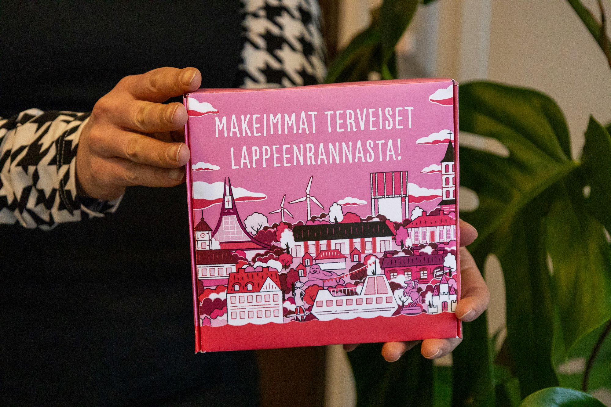 Henkilö pitää kädessään laatikkoa, jossa on piirroskuva Lappeenrannasta ja teksti Makeimmat terveiset Lappeenrannasta!