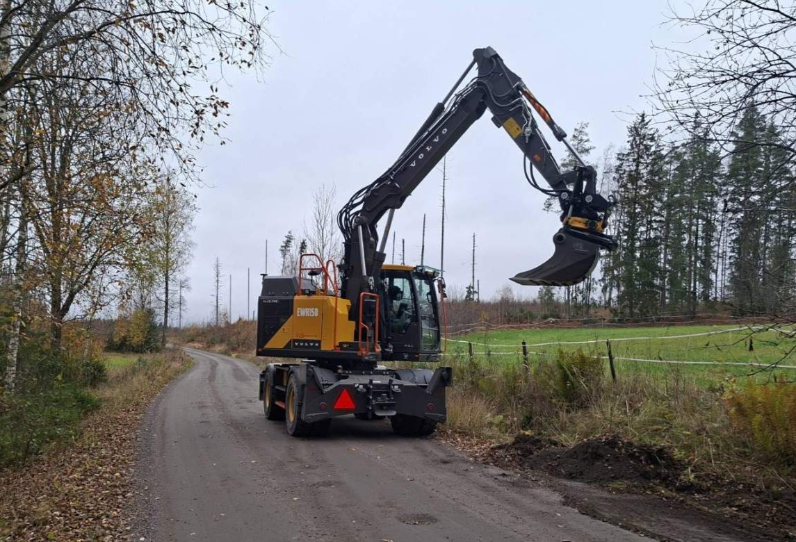 Täyssähkökaivinkone työssä hiekkatien varressa maaseudulla.