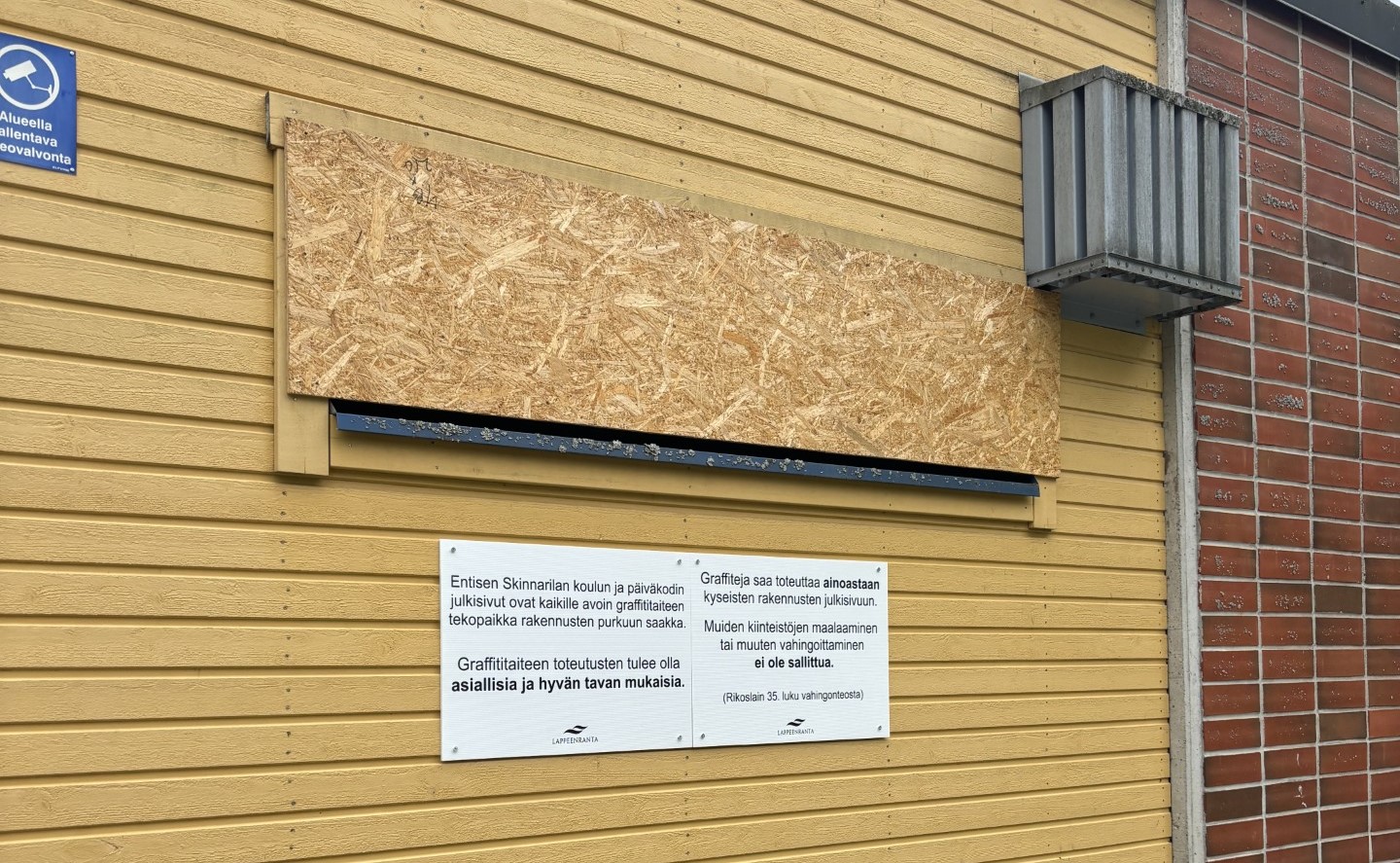 Keltainen seinä, johon on kiinnitetty Lappeenrannan kaupungin logolla varustettu kyltti, jossa on tekstinä: Entisen Skinnarilan koulun ja päiväkodin julkisivut ovat kaikille avoin graffititaiteen tekopaikka rakennusten purkuun saakka. Graffititaiteen toteutusten tulee olla asiallisia ja hyvän tavan mukaisia. Graffiteja saa toteuttaa ainoastaan kyseisten rakennusten julkisivuun. Muiden kiinteistöjen maalaaminen tai muuten vahingoittaminen ei ole sallittua (Rikoslatin 35. Luku vahingonteosta).