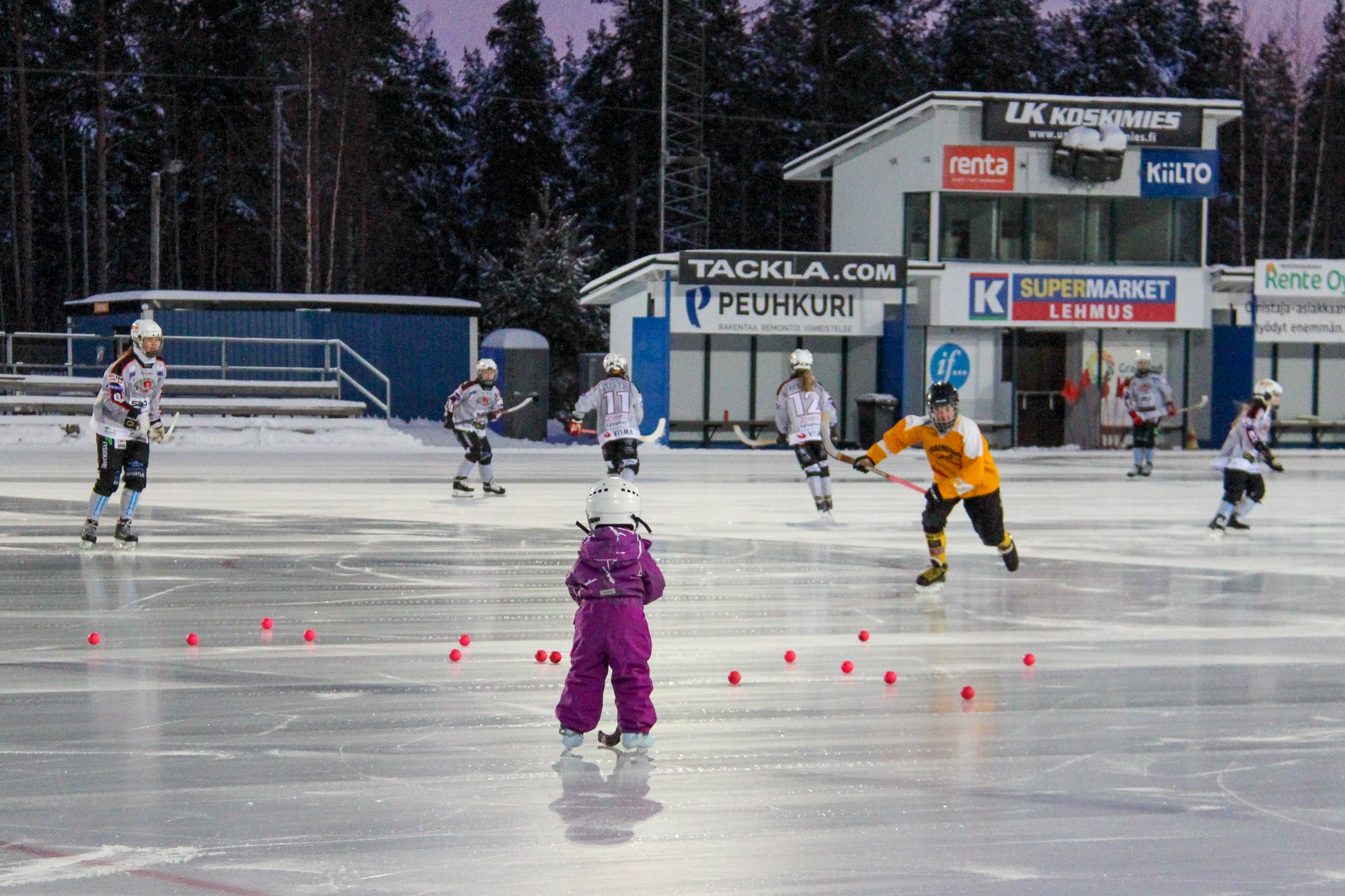 Eri ikäisiä lapsia luistelemassa tekojäällä.