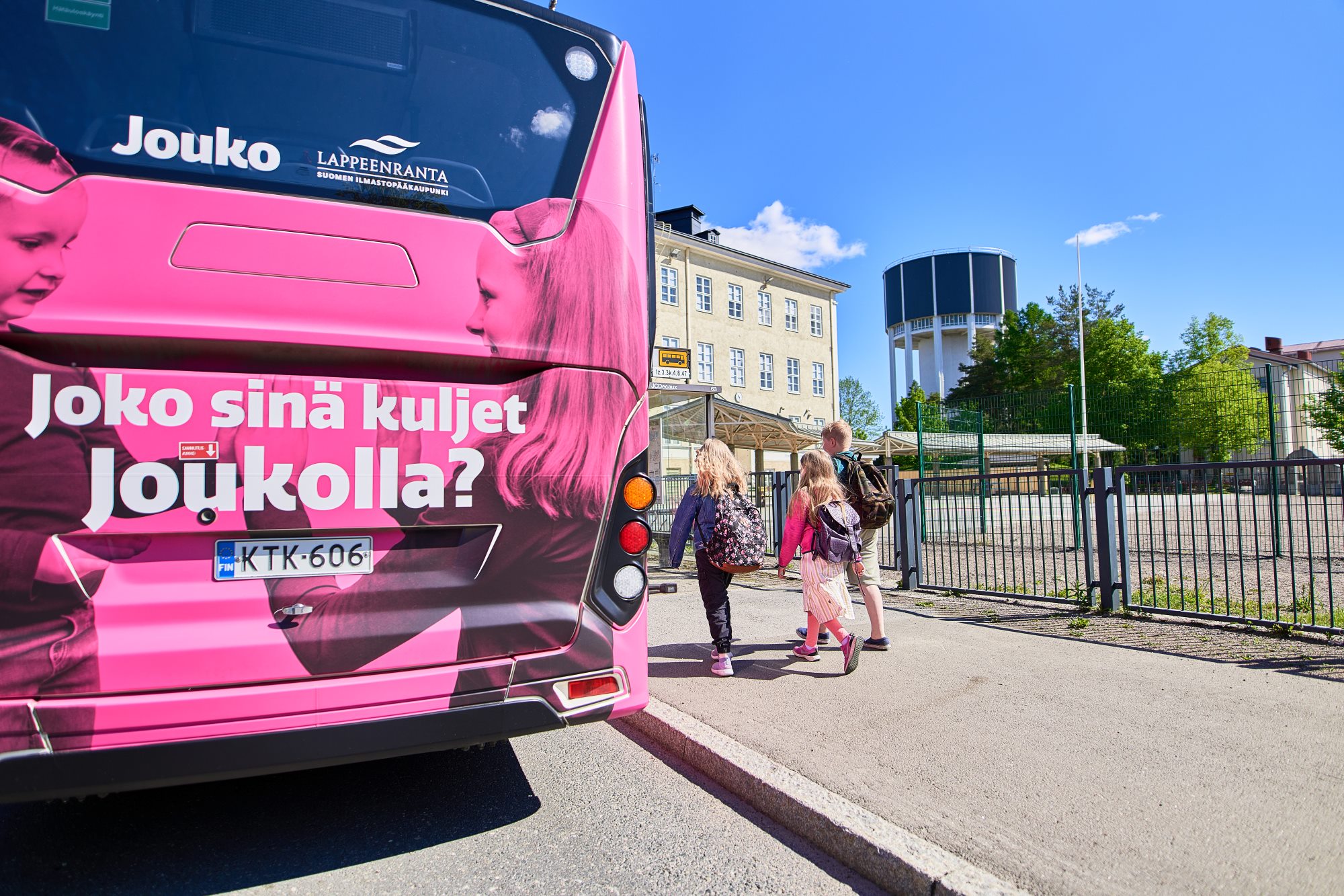 Lappeenrannan joukkoliikenteen linja-auto pysäköitynä kadun varteen sekä lapsia menossa bussin kyytiin.