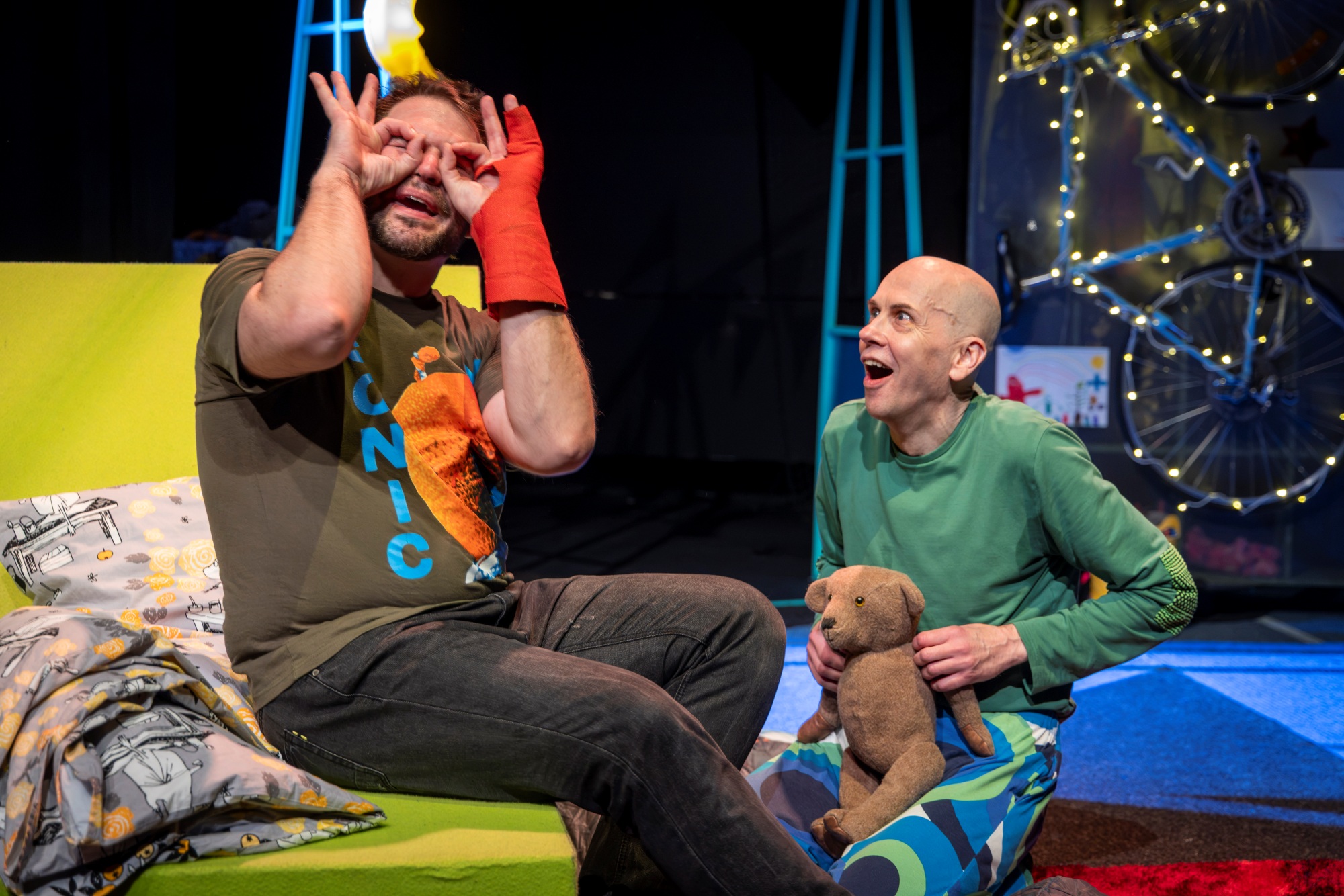 Kohtaus Lappeenrannan kaupunginteatterin näytelmästä Vanhempainilta. Isän hahmo on nostanut sormensa kiikareiksi kasvoille, lapsen hahmo katsoo tätä innoissaan nallekarhu sylissä. 