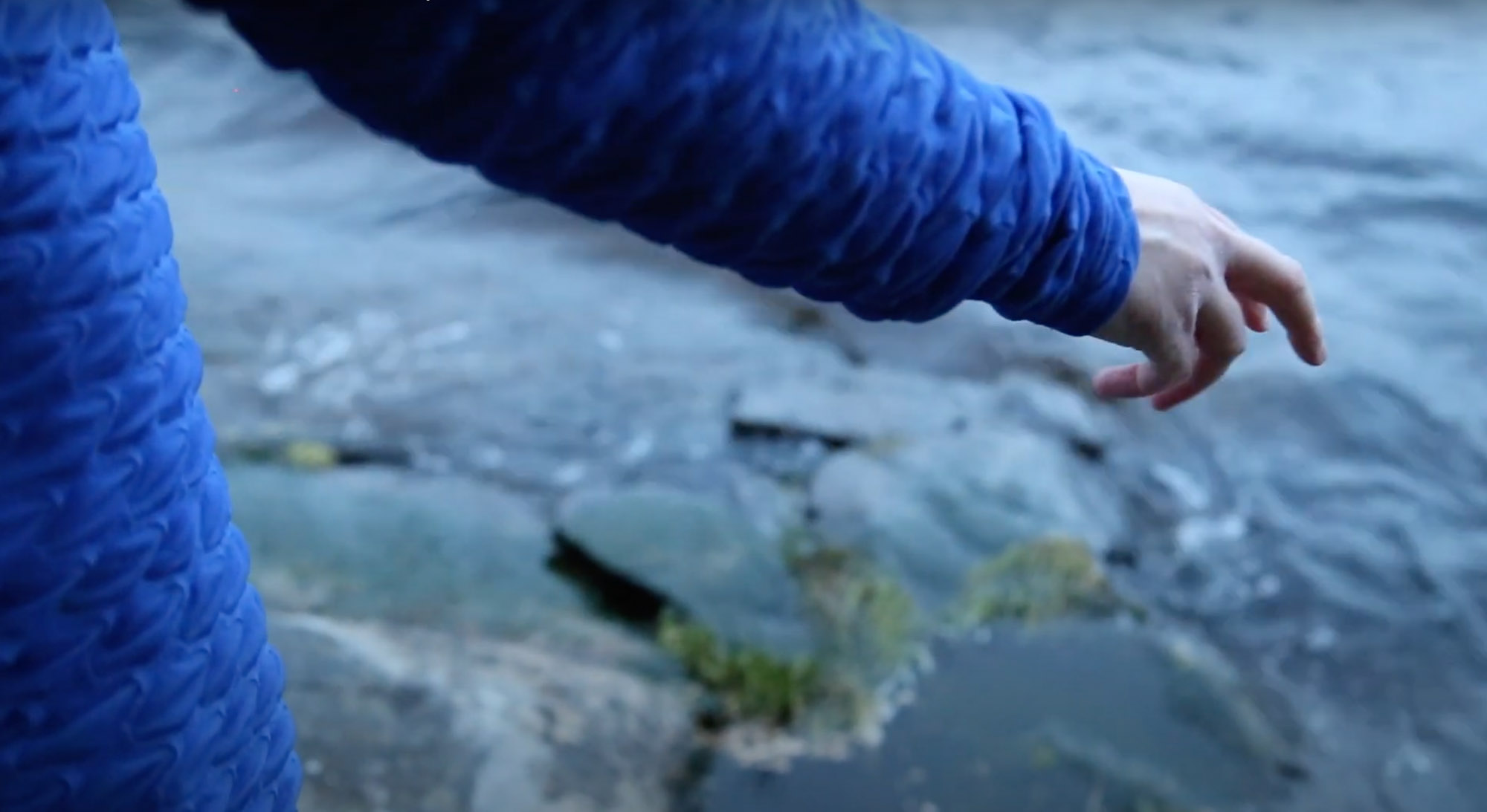 Lähikuva virtaavasta vedestä, jota ihmisen käsi melkein koskettaa.