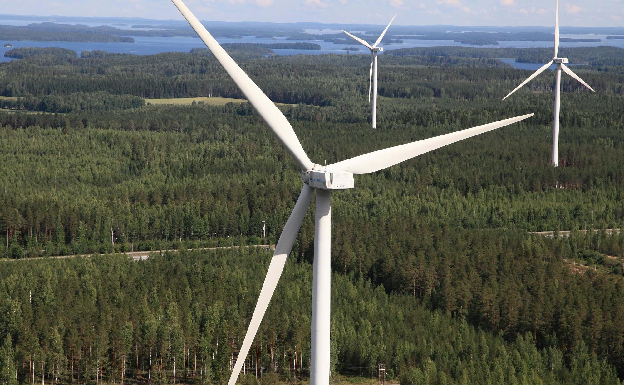 Tuulivoimaloita, taustalla metsää ja järvimaisemaa.